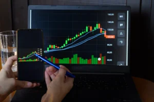 Forex trader studying candlestick chart with moving averages and indicators on laptop and phone screen in 2025.