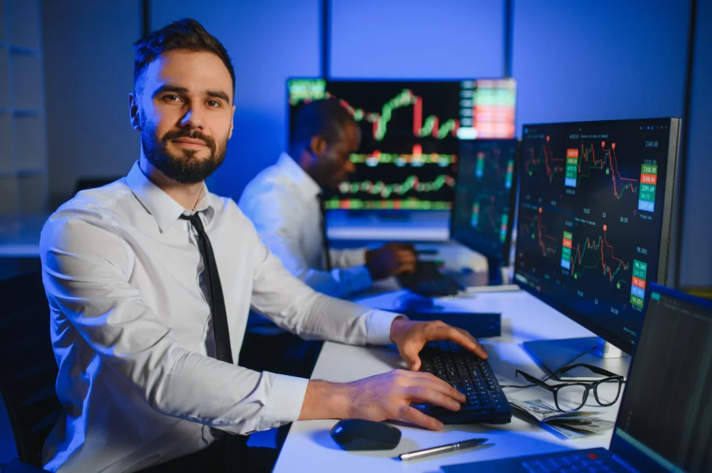 Forex traders working in a modern trading room, analyzing market charts and focusing on trader longevity through disciplined strategy.