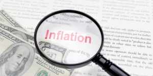 Magnifying glass showing the word inflation over US dollar bills, representing inflation and interest rates in forex markets 2025.