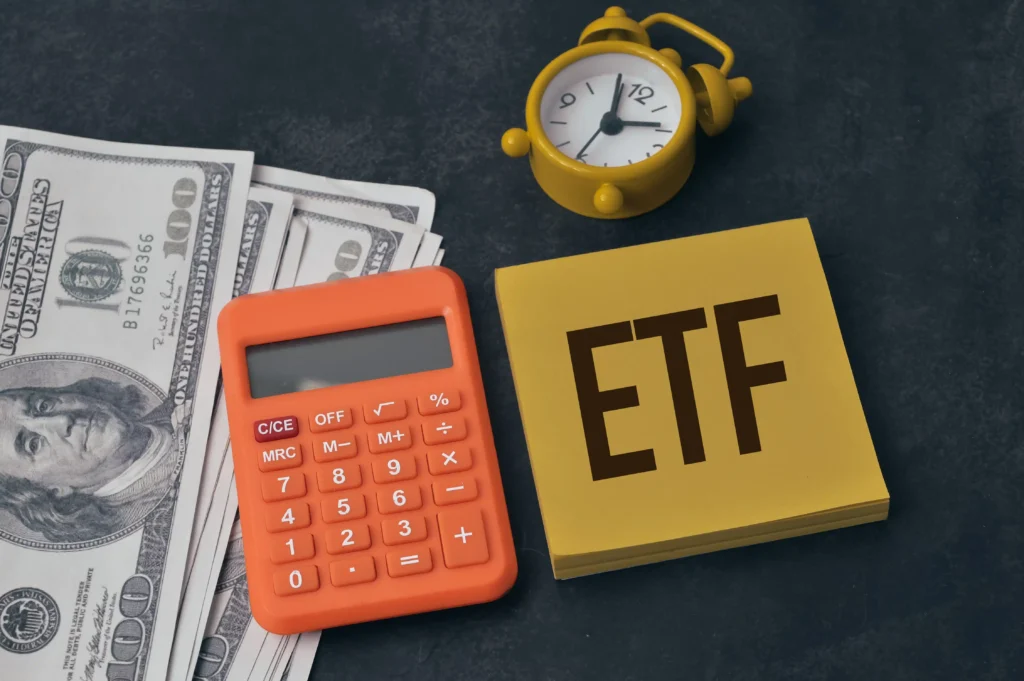 Calculator, clock, and dollar bills beside a notepad with ETF written — symbolizing Currency ETFs and investing.