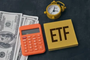 Calculator, clock, and dollar bills beside a notepad with ETF written — symbolizing Currency ETFs and investing.
