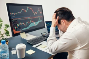 Frustrated forex trader watching multiple charts after overtrading losses