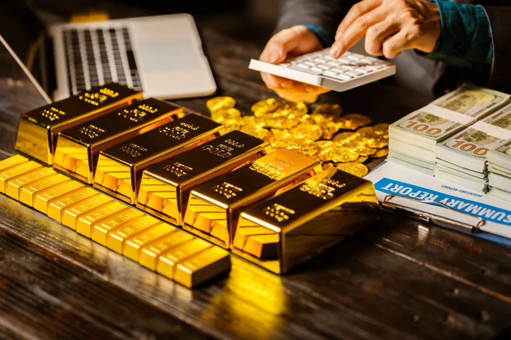 Gold bars, gold coins, and cash on a table representing wealth and safe-haven assets.