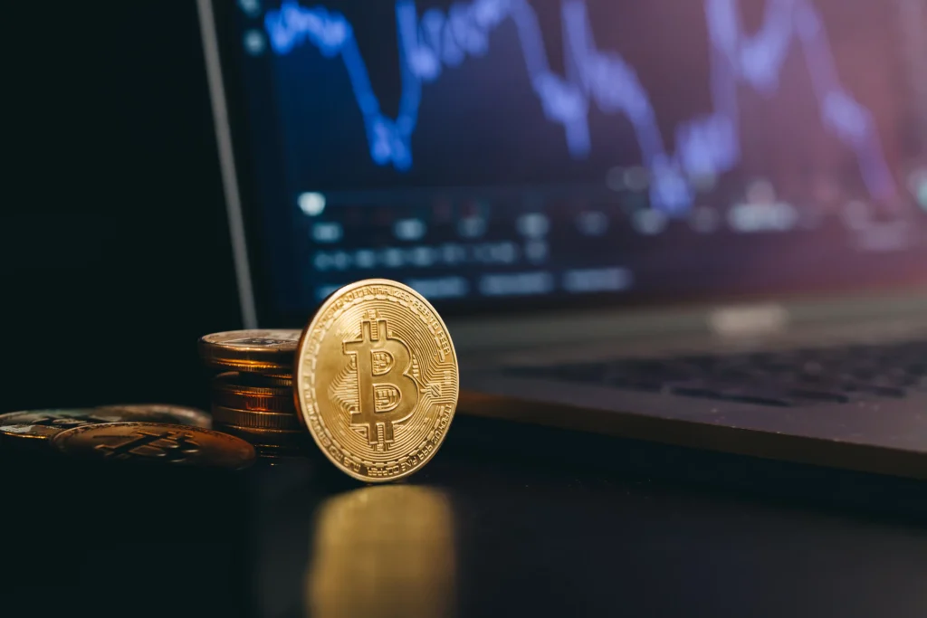 Bitcoin coin placed near a laptop showing market charts during active trading.