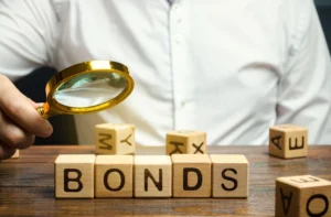 Magnifying glass examining wooden blocks spelling the word bonds, symbolizing how bond yields influence forex markets.