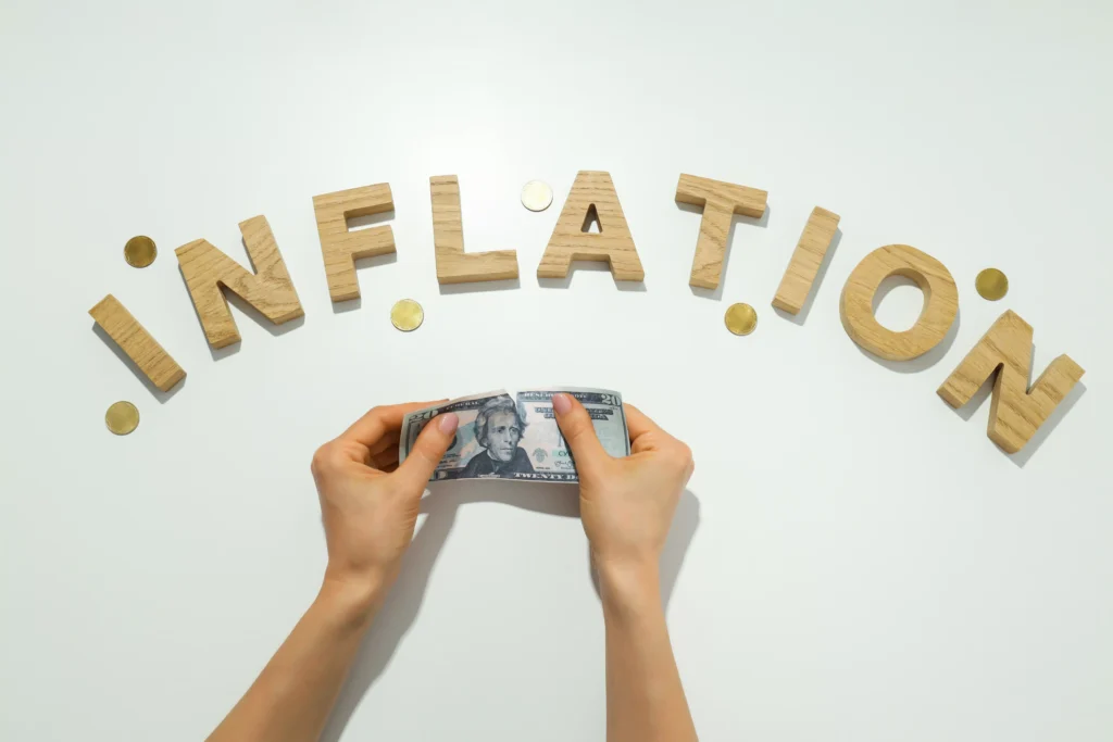 Hands holding a dollar bill under the word inflation made of wooden letters with coins, symbolizing rising prices and currency value decline.