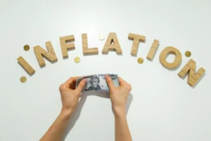 Hands holding a dollar bill under the word inflation made of wooden letters with coins, symbolizing rising prices and currency value decline.