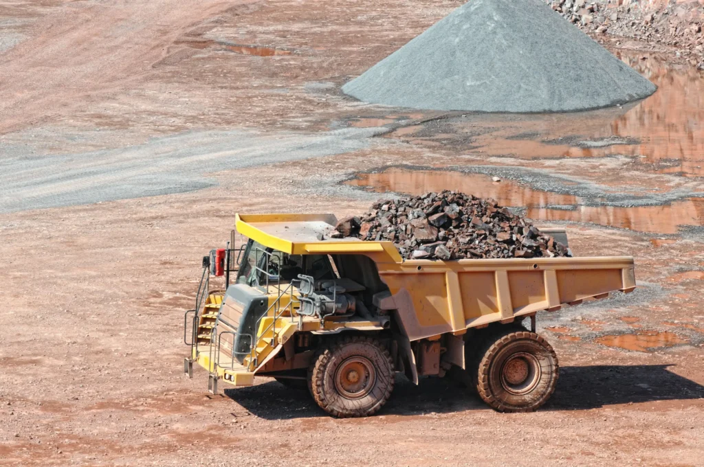 A large mining truck transporting rare-earth ore at an active quarry site, representing the extraction process vital to global trade and industrial growth.