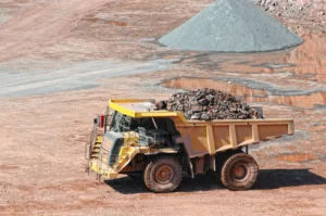 A large mining truck transporting rare-earth ore at an active quarry site, representing the extraction process vital to global trade and industrial growth.