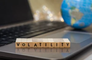 Volatility word blocks placed on a laptop with a blurred globe in the background, representing low volatility risks in global markets.