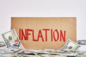 Inflation concept with US dollar bills scattered around a cardboard sign reading inflation.