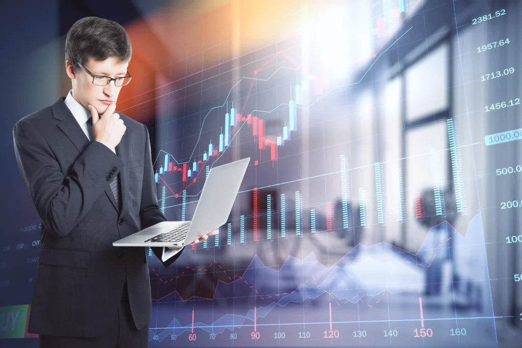 Business analyst studying order flow trading data on a laptop with financial charts in the background.