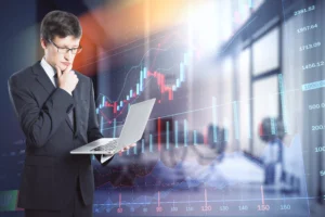 Business analyst studying order flow trading data on a laptop with financial charts in the background.