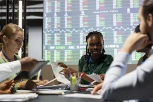 Team of financial analysts reviewing charts and market data during after-hours trading session with stock boards in background.
