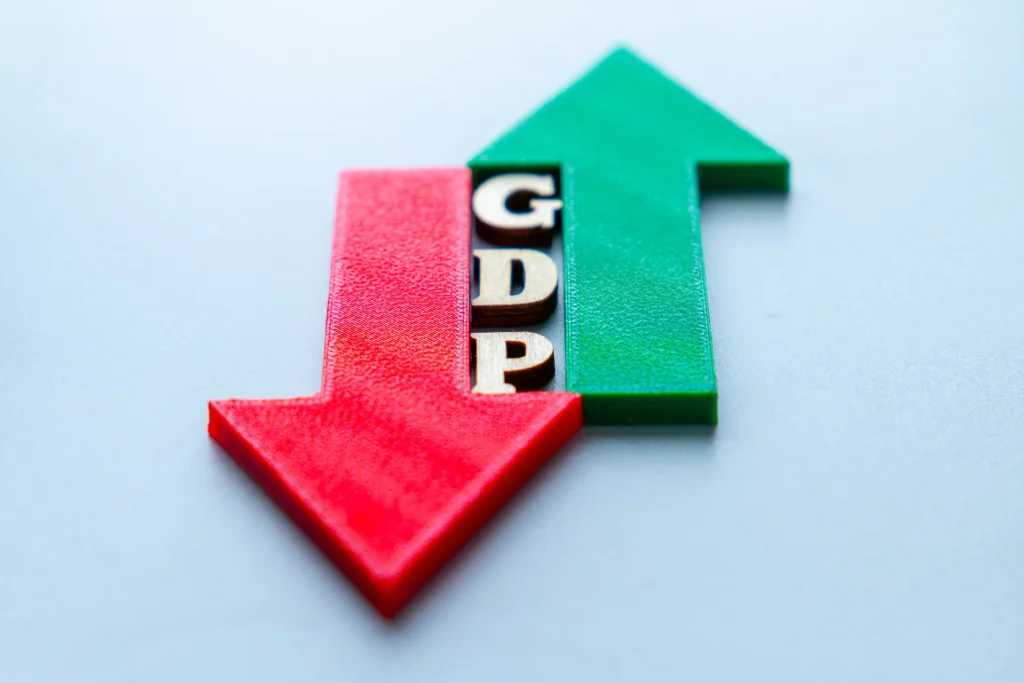 Red downward arrow and green upward arrow with wooden GDP letters symbolizing economic rise and fall.