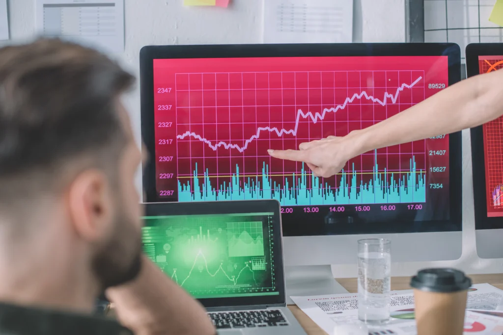 Analyst pointing at trend chart on trading screen while discussing Exponential Moving Average signals.