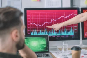 Analyst pointing at trend chart on trading screen while discussing Exponential Moving Average signals.