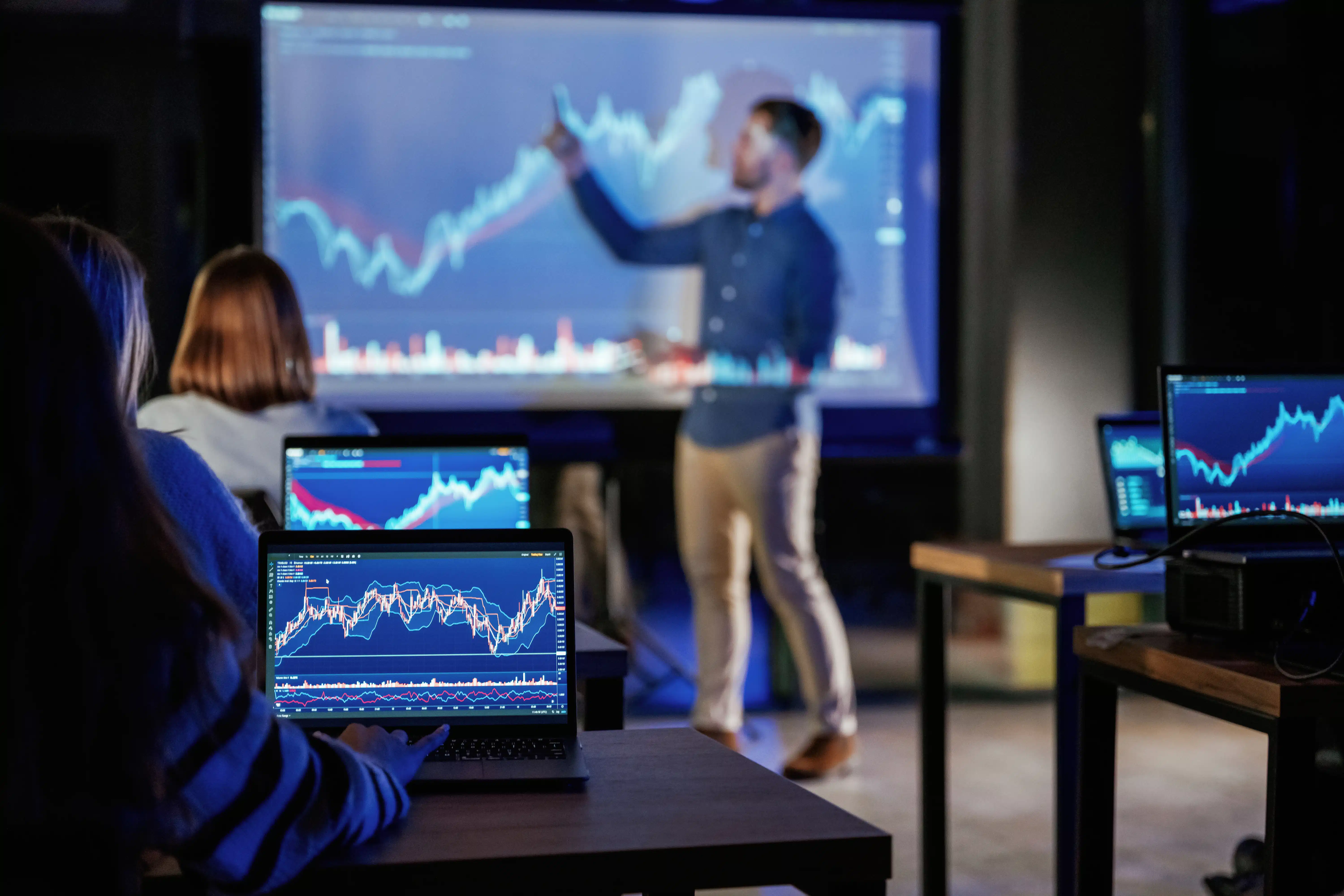 “Instructor explaining Quant Trading Models with stock charts displayed on laptops and screen in 2026.”